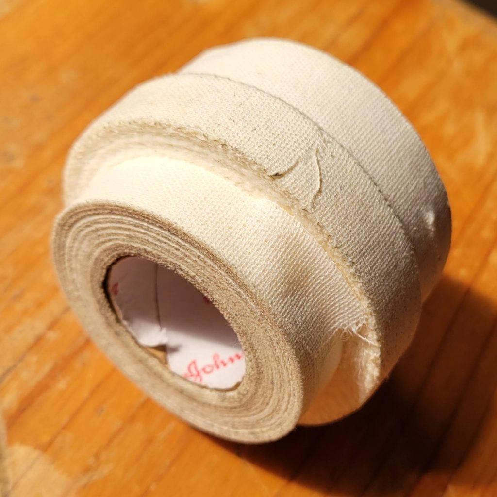 Johnson and Johnson finger tape roll with strips of various sizes torn into the roll for finger taping.